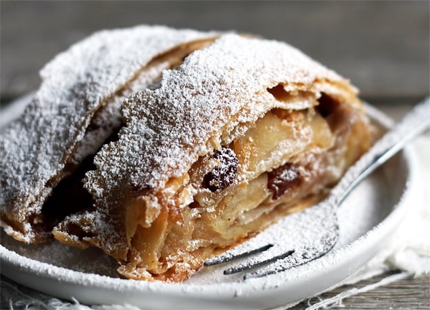 image of the apple strudel or apfelstrudel with icing sugar covered served on a plate with a cake fork
