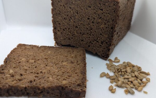 Freshly baked deep earth rye black bread (pumpernickel) with a rich, dark color and dense texture, made with 100% rye flour and sunflower seeds for a hearty, flavorful taste