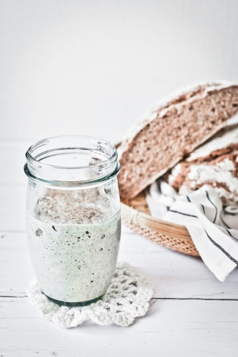 a glass jar with sourdough starter in it next to a loaf of bread
